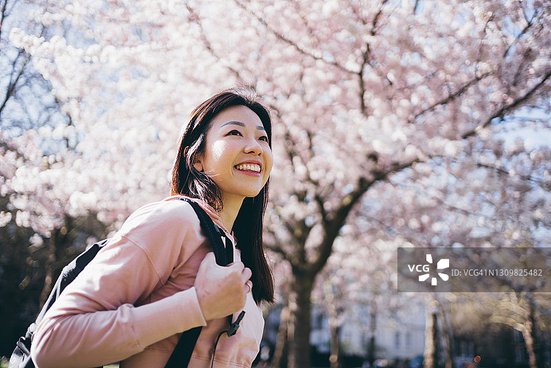 亚洲年轻开朗的女人在公园里盛开的樱桃树前仰望天空图片素材