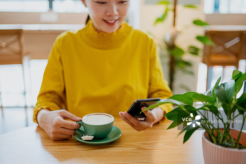 年轻的亚洲女子在咖啡馆用智能手机图片素材