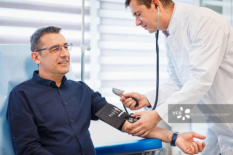 男人坐在医生的办公室里，医生在测量他的血压和心率图片素材