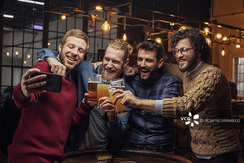 酒吧里的快乐聚会:一群快乐的年轻人边喝啤酒边自拍图片素材