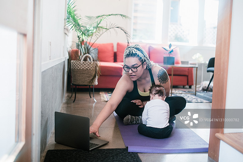 妇女在家锻炼与婴儿儿子使用网络课程图片素材