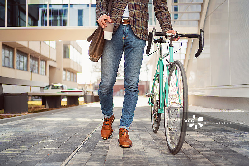 一个面目全非的时髦男人，端着一杯咖啡，骑着自行车，走路图片素材
