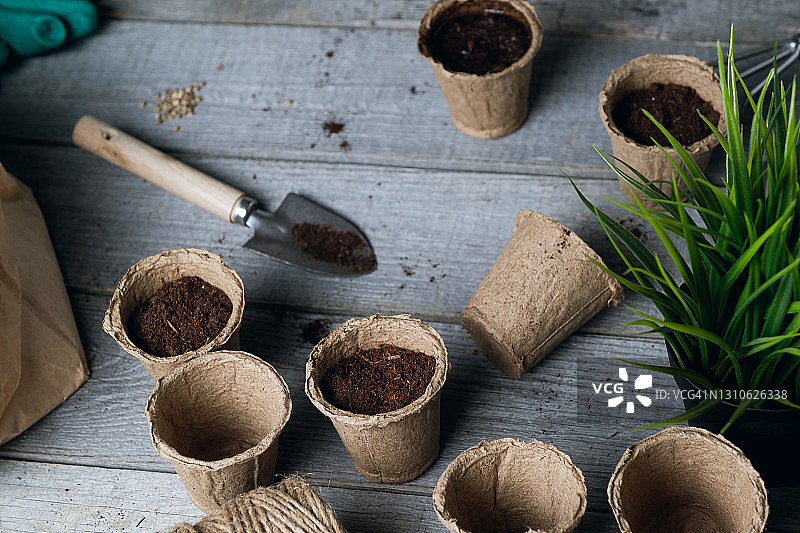 泥炭罐，空的，装满土或黑土的泥炭罐。园艺工具，一个小铲子，一个耙子。在木桌的背景上种植和播种鲜花、植物或蔬菜。种植有机农产品。空间的副本。图片素材
