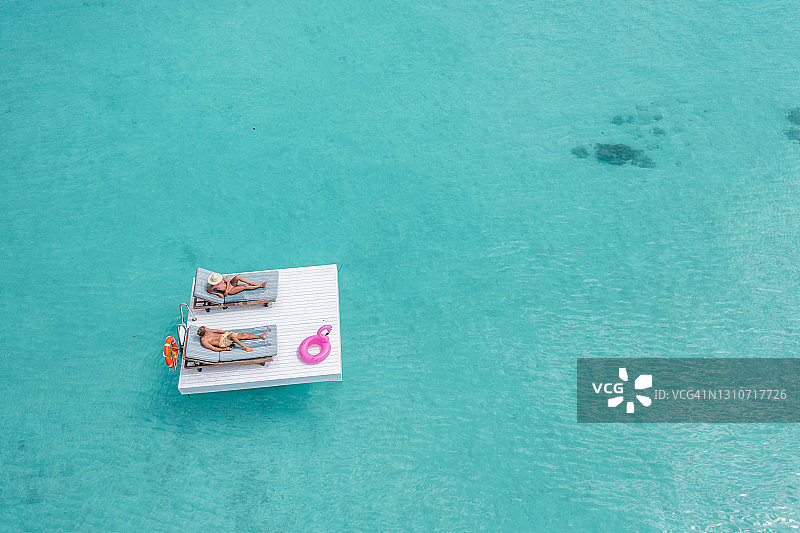 一对夫妇在热带泻湖上方的木筏上放松，无人机视图图片素材