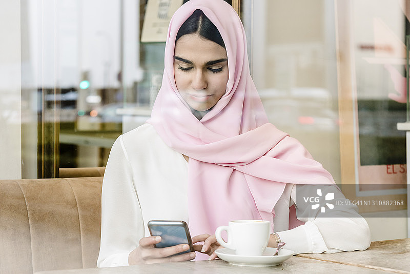 一名年轻的阿拉伯女子坐在咖啡店里查看她的社交网络图片素材