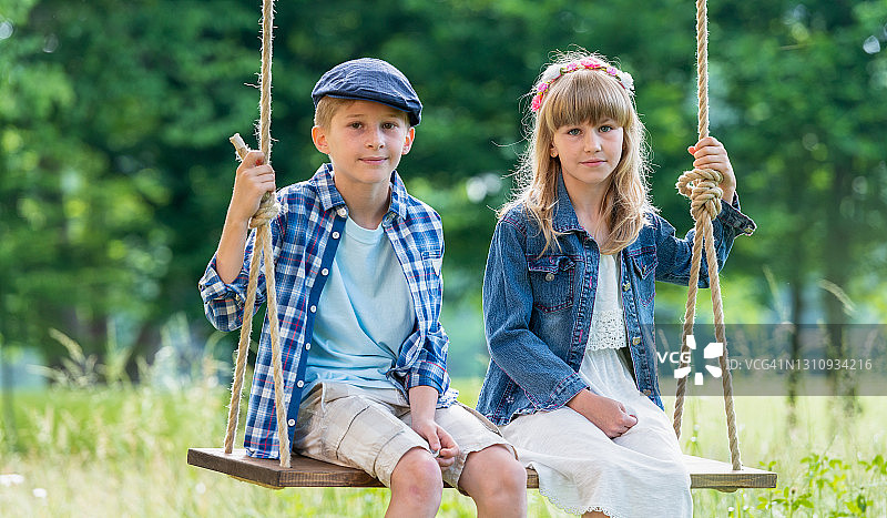 男孩和女孩坐在森林里的秋千上图片素材