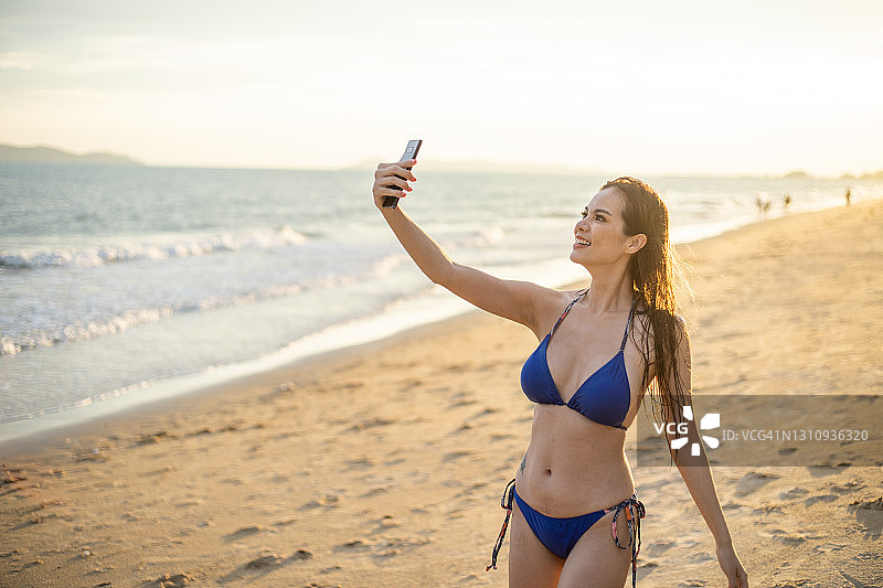 年轻女性在海滩上自拍和视频电话与比基尼。图片素材