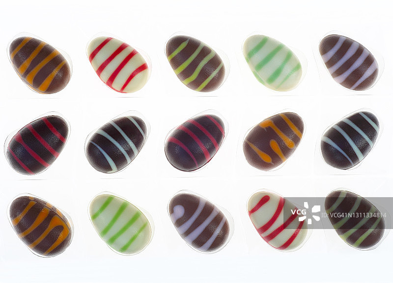 三排彩色的，条纹的，白色的巧克力复活节彩蛋。图片素材