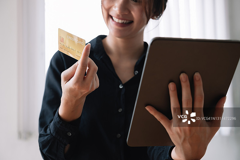 亚洲妇女使用笔记本电脑和信用卡在家里购物进行在线支付。图片素材