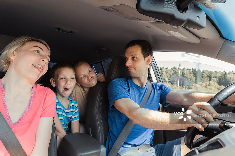 一个年轻快乐的家庭和两个孩子的滑稽面孔是玩顽皮的公路旅行在汽车图片素材