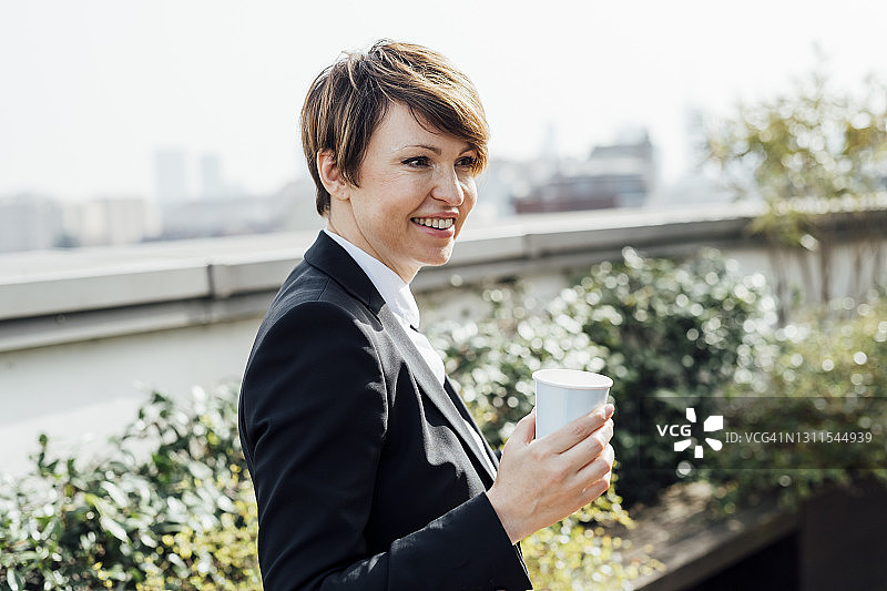 微笑的女企业家拿着一次性咖啡杯，但眼睛看向别处图片素材