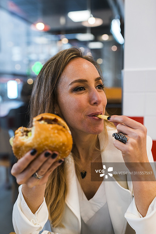 漂亮的职业女性一边吃汉堡一边看别处图片素材