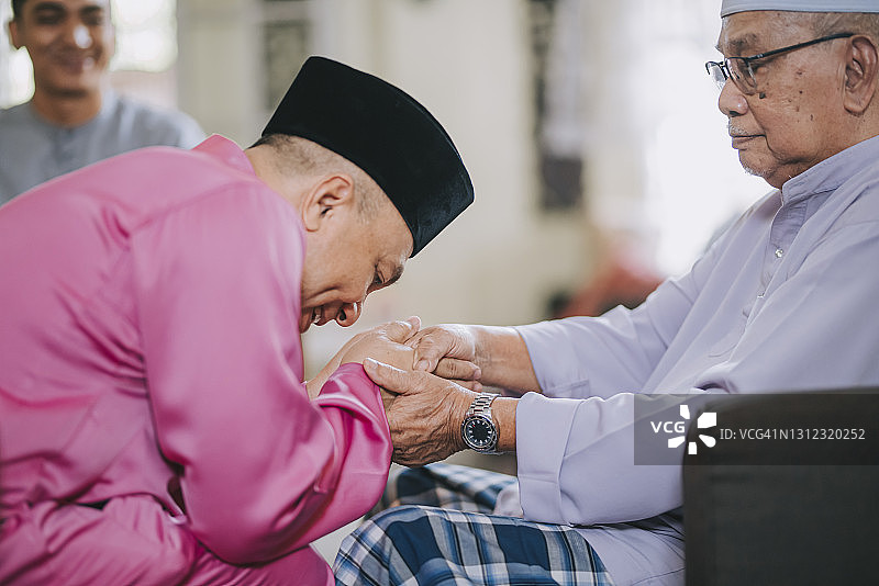 一个马来穆斯林儿子，穿着传统服装向他的父亲道歉图片素材