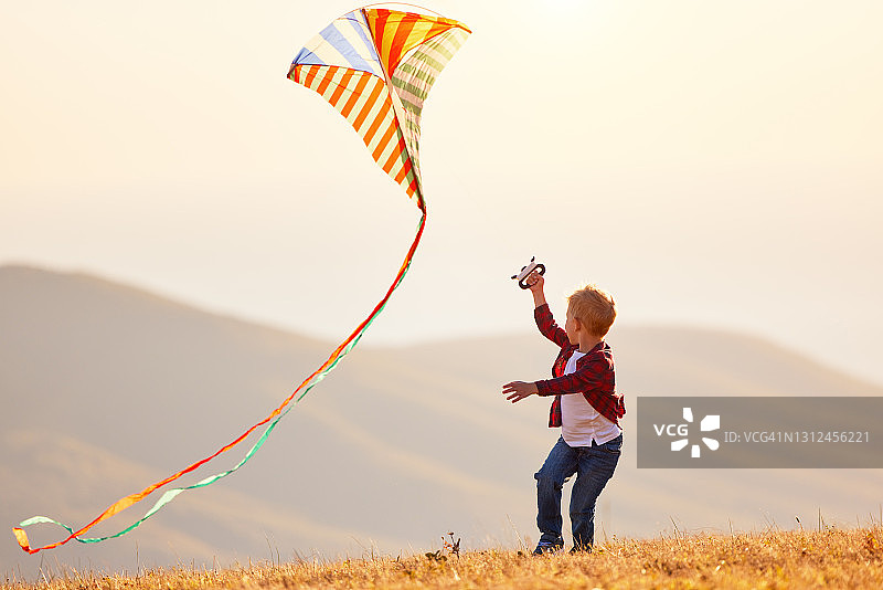 快乐的小男孩和风筝在日落户外图片素材