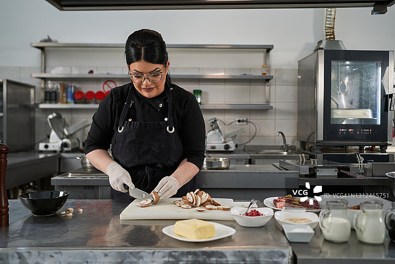 穿着制服的女厨师在餐厅的商业厨房里切菜，为以后的准备工作做准备图片素材
