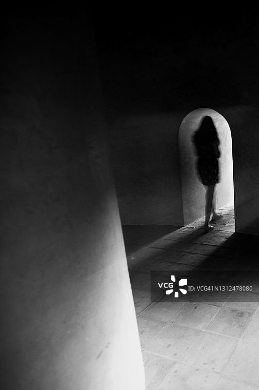 一个不知名的女性独自走在黑暗古老的地下室里。图片素材