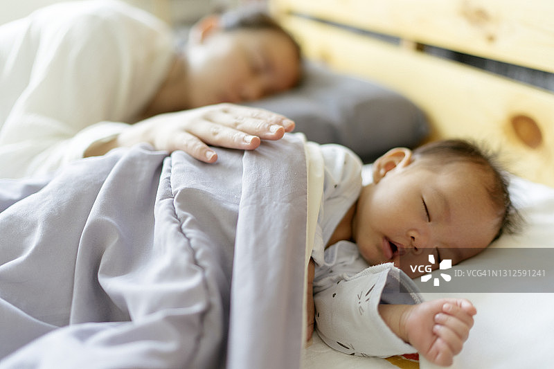 清晨，亚洲新生女婴和妈妈一起睡在舒适的床上图片素材