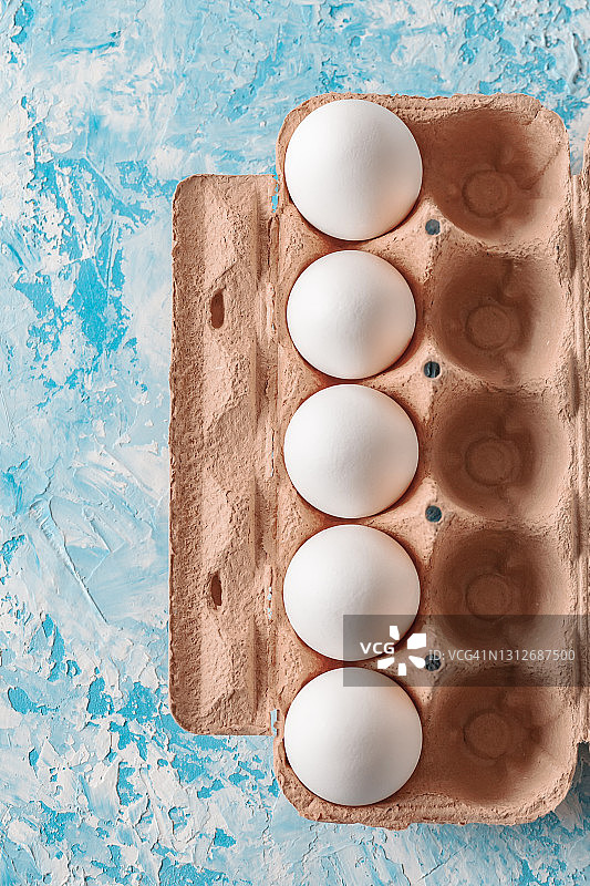 高角度的观点，白色的鸡蛋在棕色的硬纸板对蓝色的背景图片素材