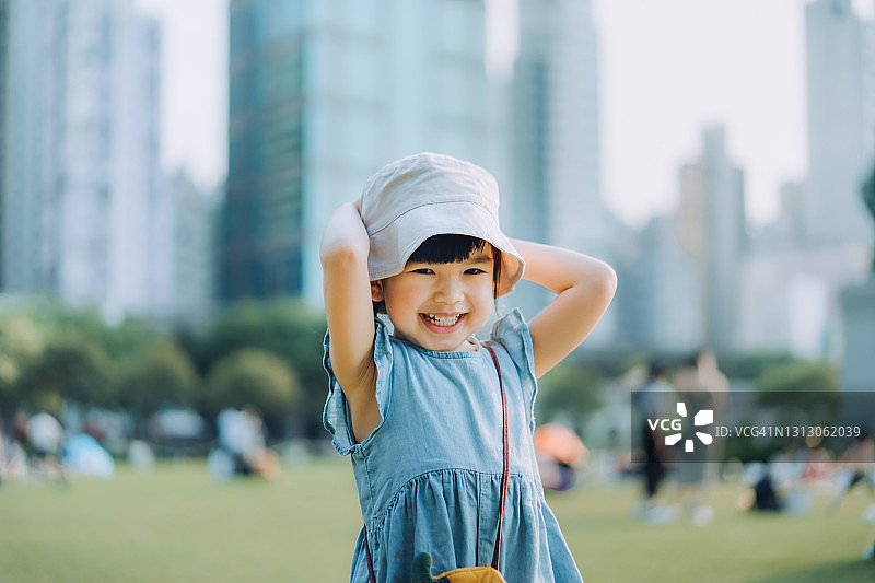 肖像快乐的小亚洲女孩玩在城市公园，快乐地微笑。享受自由和自然之美。以现代城市景观为背景图片素材