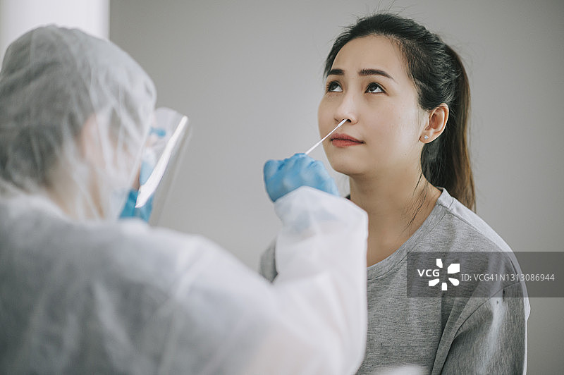 亚洲华裔女医生带着个人防护装备从患者的冠状病毒检测中提取鼻拭子。穿着防护服的医护人员拿棉签做冠状病毒测试，可能是一名受感染的妇女图片素材