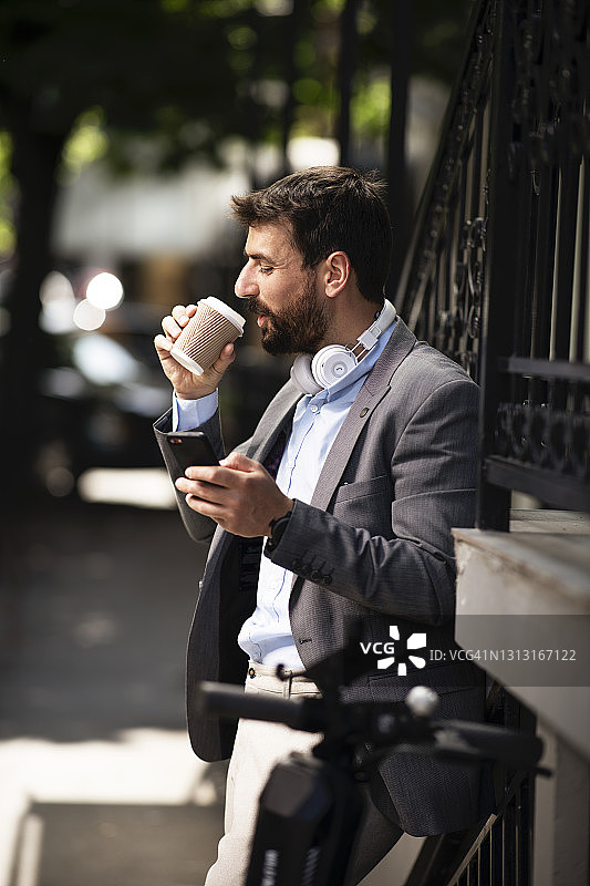 年轻的商人站在城市的街道上喝着咖啡。库存图片图片素材