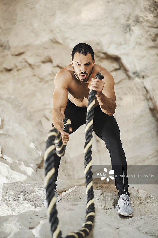 一位年轻的男运动员正在用格斗绳练习。被大自然和岩石包围着。图片素材