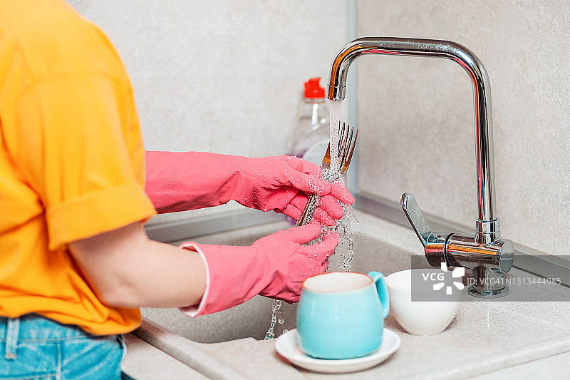 清洗。一位戴着粉红色橡胶手套的妇女正在洗盘子。从肩膀看图片素材