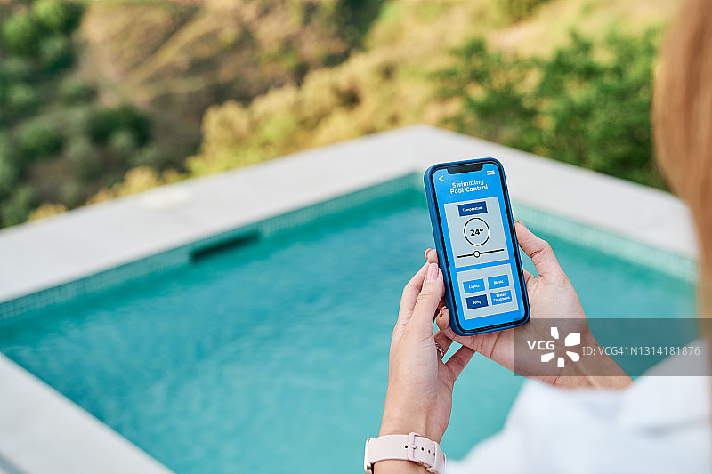 一名女子用智能手机上的应用程序控制游泳池的水温。图片素材