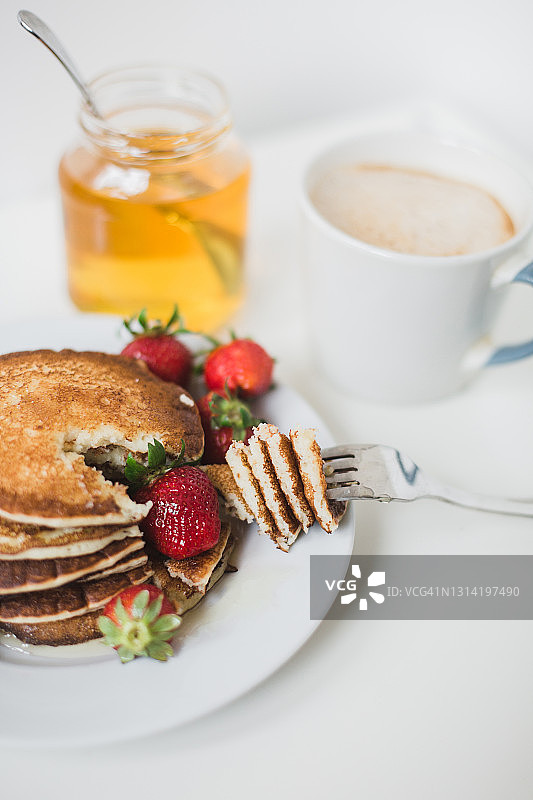 美丽的早餐煎饼，新鲜的草莓和蜂蜜，一杯咖啡在白色的背景图片素材