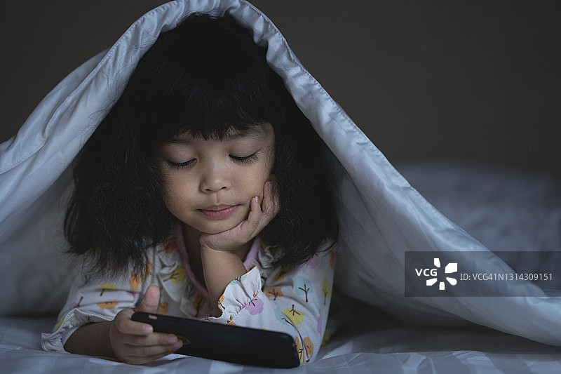 亚洲小女孩在深夜玩智能手机和游戏。图片素材