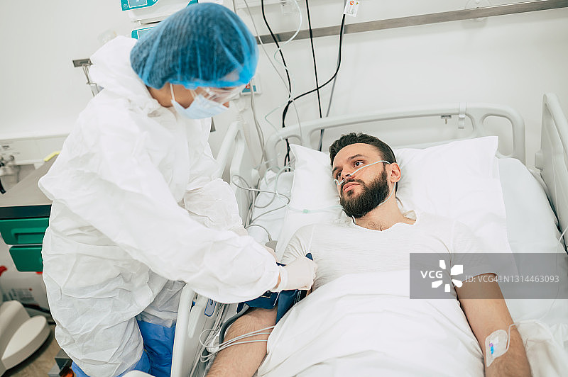 新冠肺炎患者在医院隔离病房，医生穿着防护服对其进行疾病治疗图片素材