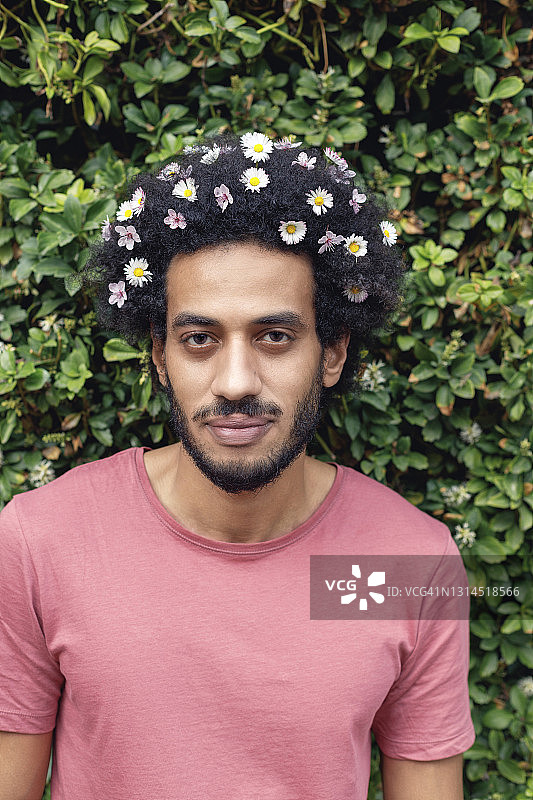 一个头发插着花的黑人青年站在植物前图片素材