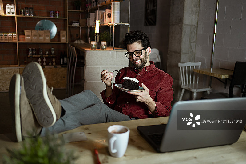 笑容可掬的商人带着笔记本电脑和咖啡在咖啡店吃着光滑的蛋糕图片素材