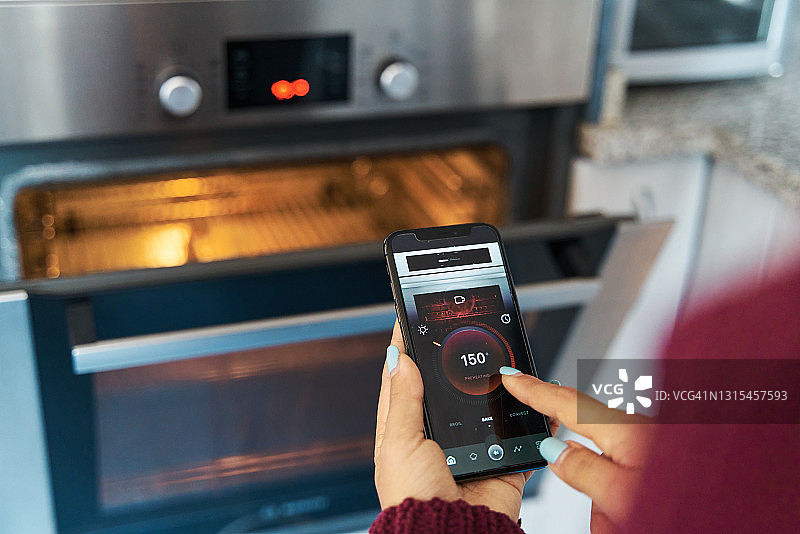 通过智能手机应用控制智能烤箱温度的女性图片素材