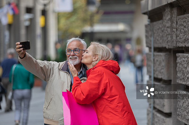 一对快乐的老年人走在街上，正朝着购物中心走去，同时在自拍。图片素材