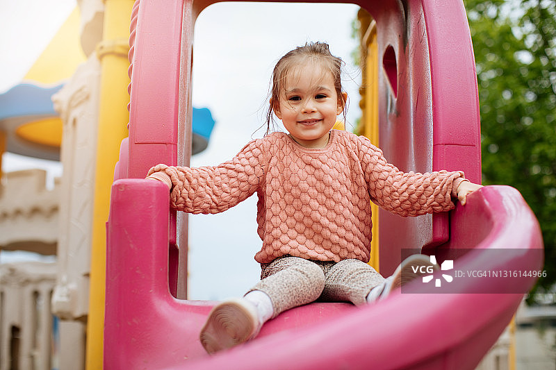 一个2-3岁的女孩滑下滑梯是非常快乐，积极的情绪图片素材