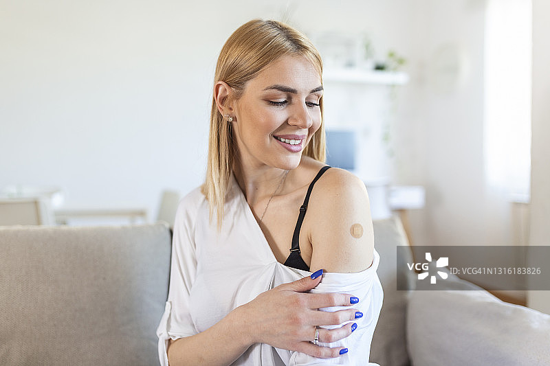 一名妇女接种疫苗后微笑的肖像。妇女按住她的衬衫袖子，并显示她的手臂与绷带接受疫苗接种后。图片素材