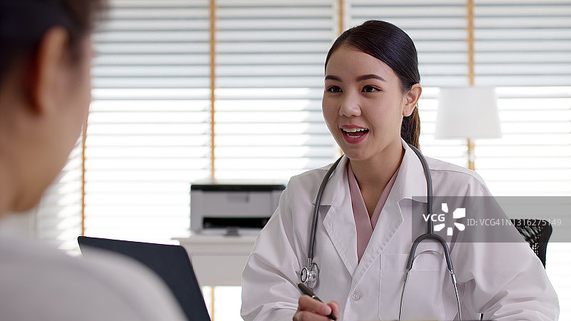 迷人的美丽年轻的亚洲医生女穿着白袍听诊器在肩上诊断与病人谈话提供帮助咨询，治疗或解释处方在办公室诊所。图片素材