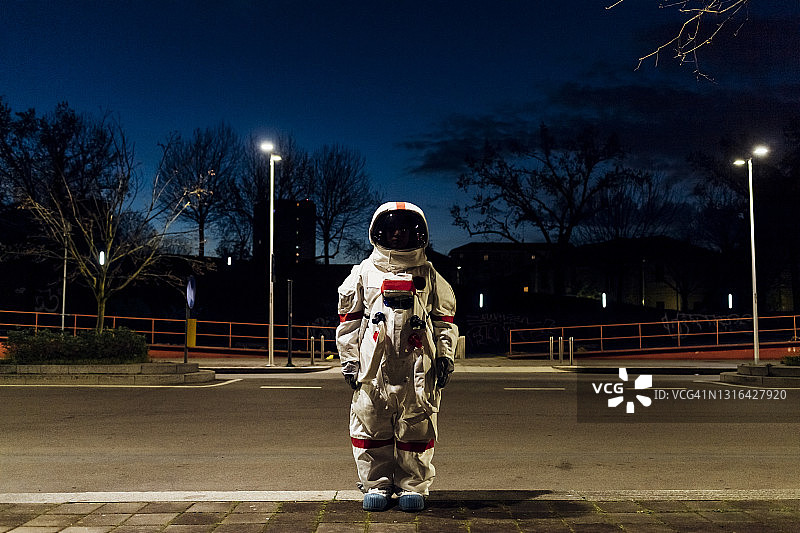 年轻的女宇航员穿着太空服晚上站在人行道上图片素材