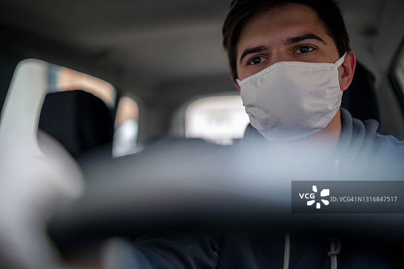 冠状病毒爆发期间，一名戴一次性医用口罩的男子在一辆汽车里图片素材