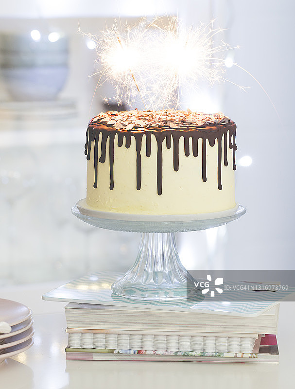 香草生日蛋糕与巧克力甘纳许，釉，和火花在一个厨房的蛋糕架上图片素材