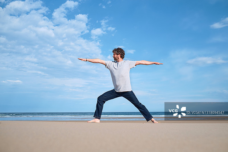 一个男人在一个阳光明媚的日子里在海滩上练习瑜伽图片素材