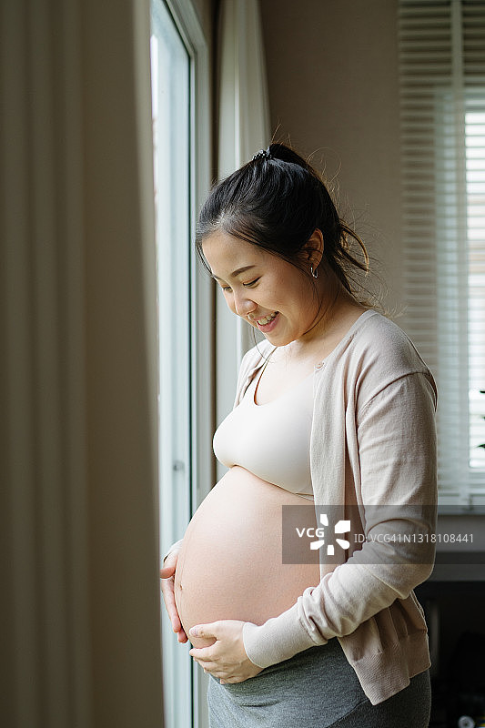年轻的亚洲怀孕女孩在家看外面的肖像图片素材