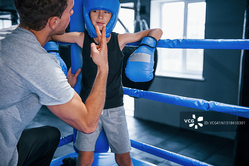 一个年轻的拳击教练正在帮助一个小男孩穿上防护服图片素材