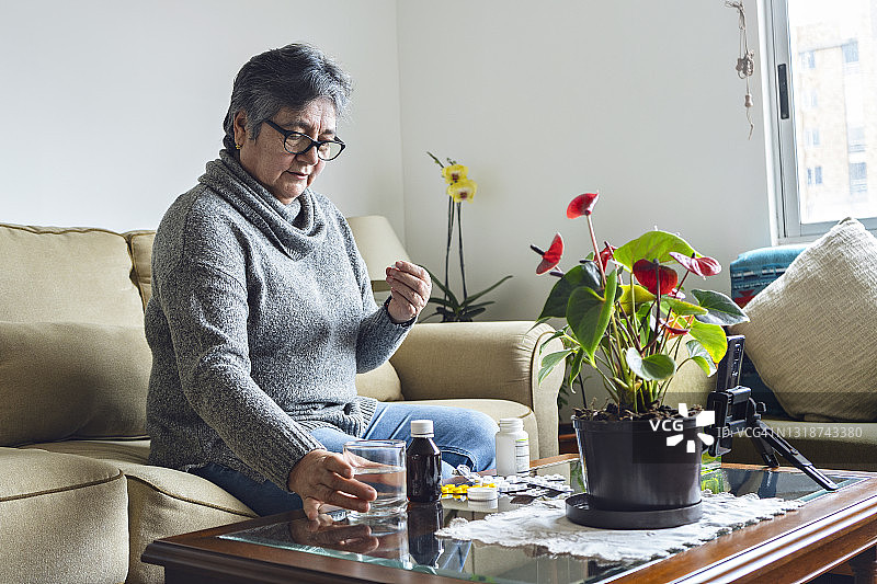 拉丁老年妇女在视频通话中照顾她的医生与她的药在桌子上的要求图片素材
