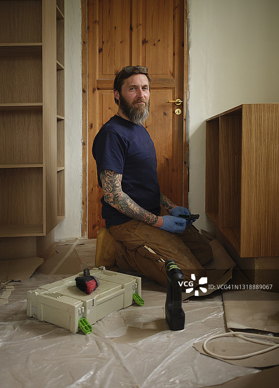 一个时髦的木匠跪在厨房的柜子旁图片素材