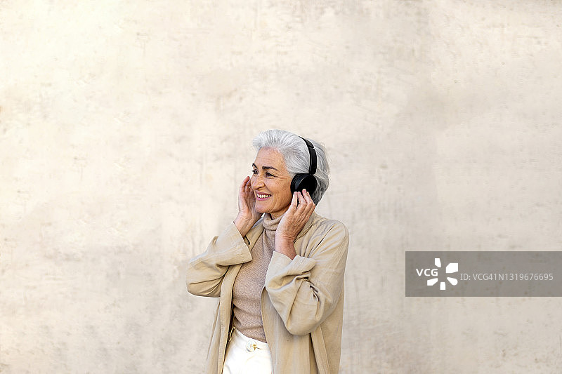 面带微笑的成熟女人在墙前戴着耳机听音乐图片素材