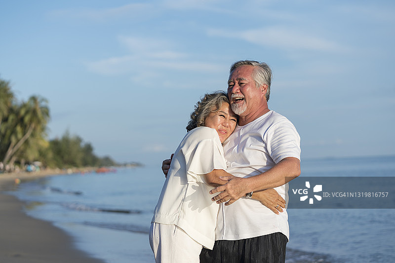 幸福微笑的资深亚洲夫妇在海滩上互相拥抱。图片素材