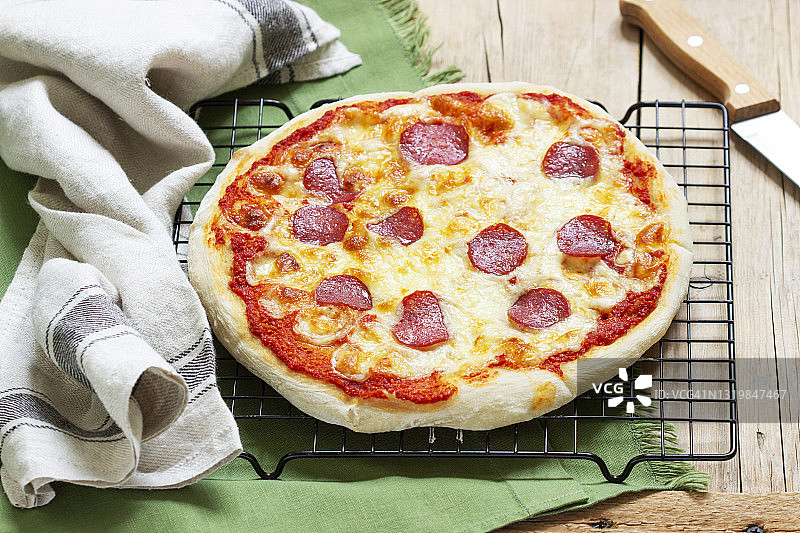 木桌上放着自制披萨，配上番茄酱、香草、香肠和奶酪。图片素材
