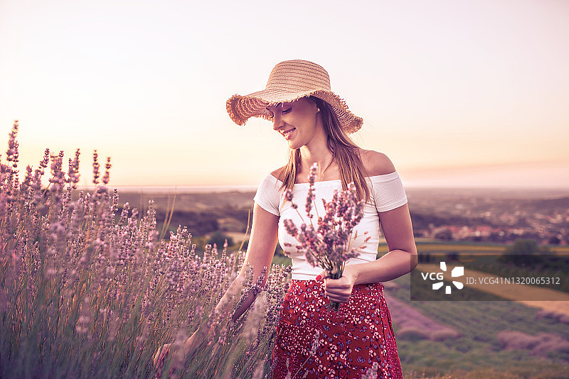 美丽的年轻女子戴着草帽在紫色的薰衣草地里图片素材